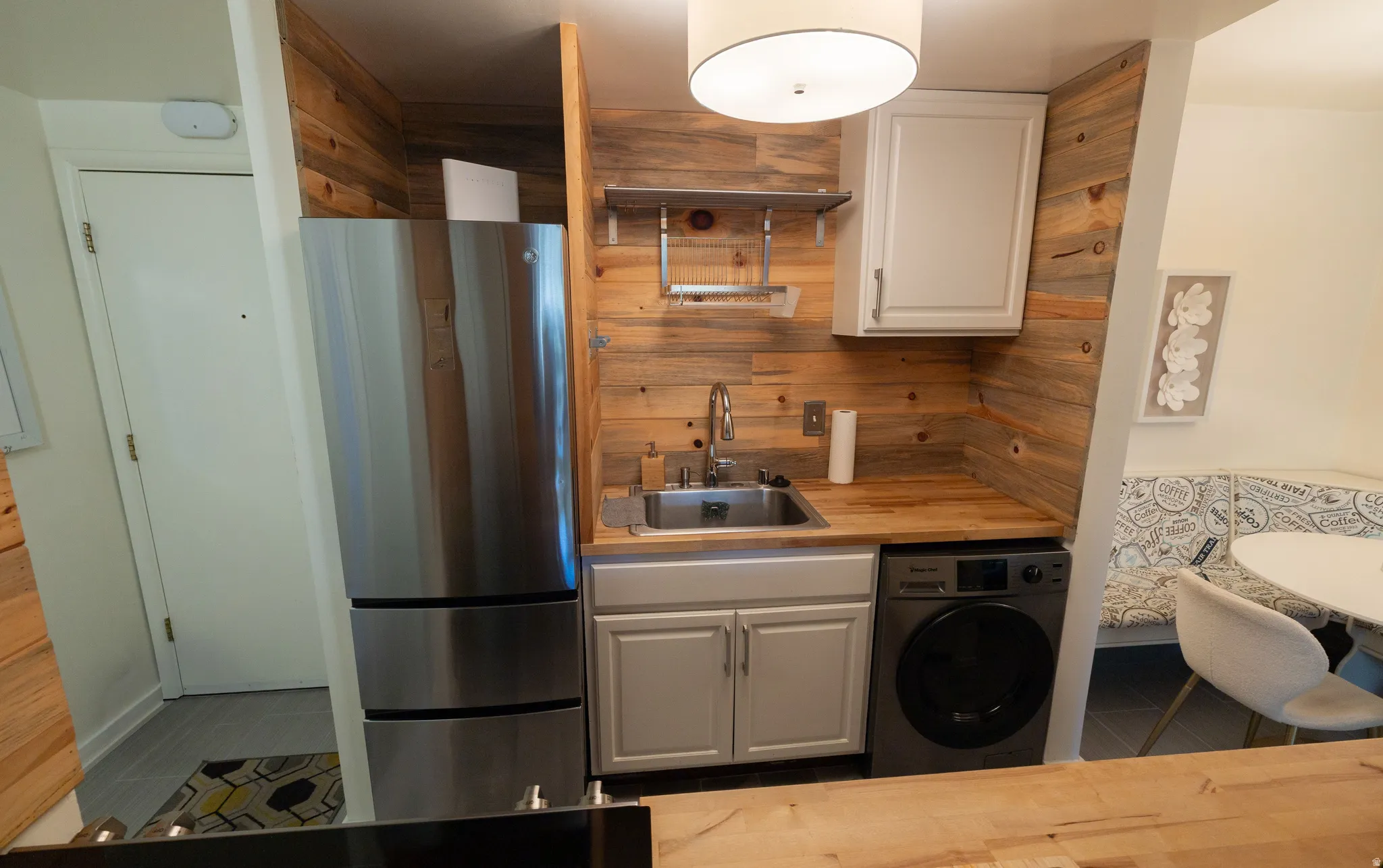 Compact kitchen featuring wood-finish paneling, stainless steel refrigerator, stainless steel sink, wood-finish countertop, and a built-in washer/dryer unit