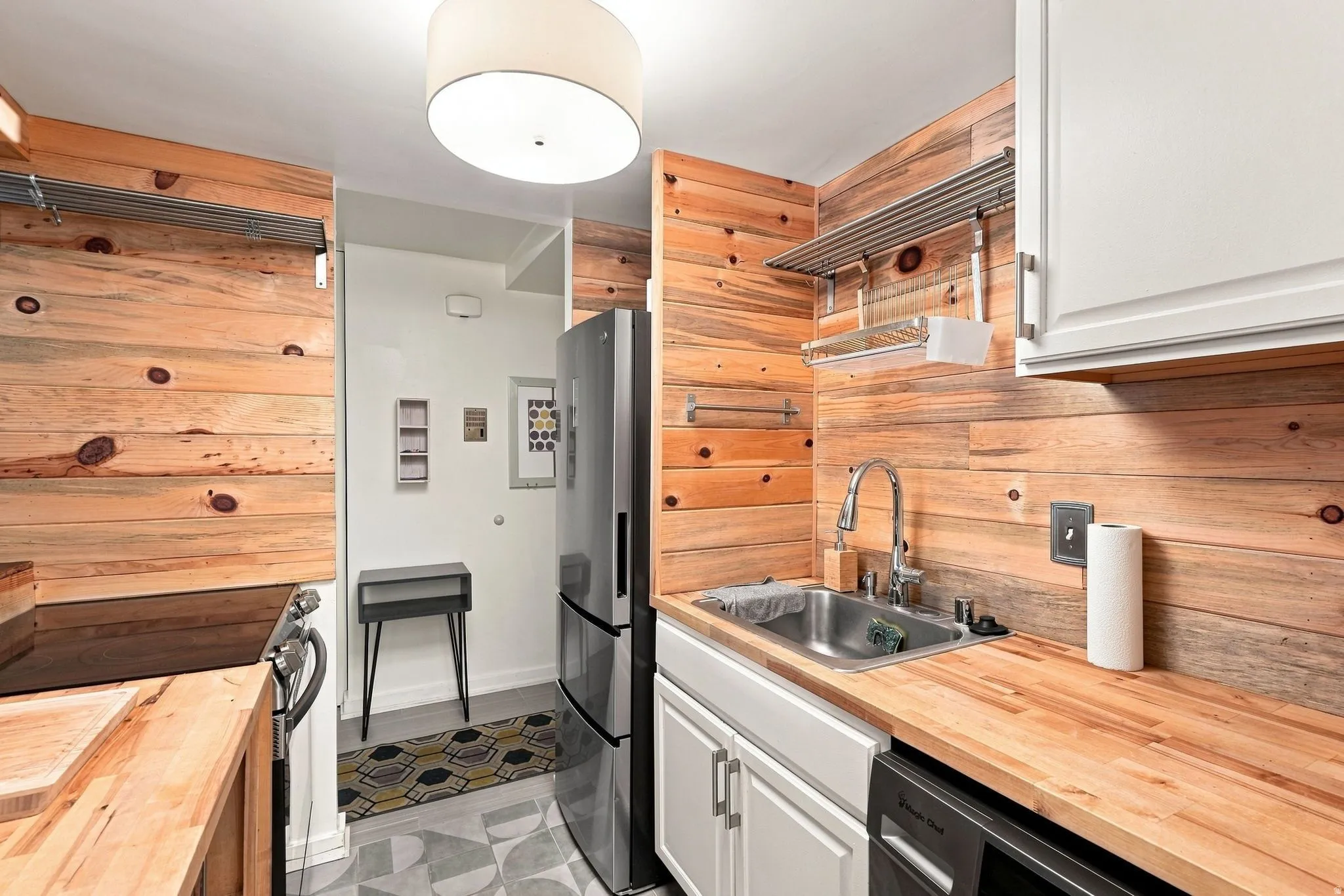Kitchen featuring wood plank walls, stainless steel sink with a gooseneck faucet, light wood countertops, white cabinetry, and stainless steel refrigerator