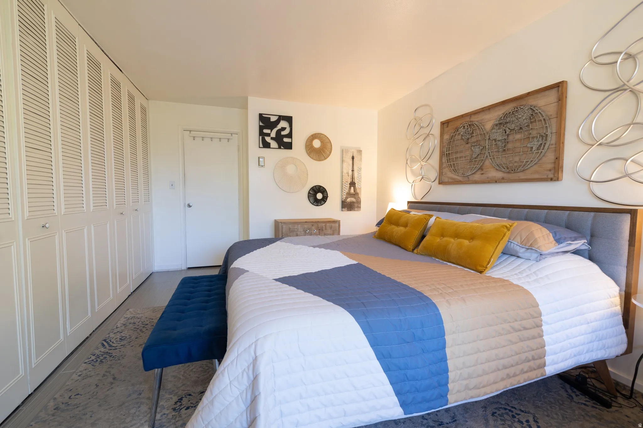 Bedroom featuring a wall of louvered closet doors, a bed with a tufted headboard, light-colored walls, and wood-finish flooring