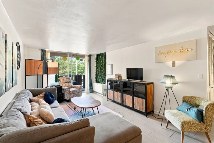 Bright, open living space featuring expansive glass sliding doors with natural light, light wood-finish flooring throughout, and a built-in media console with wood cabinetry and woven basket storage
