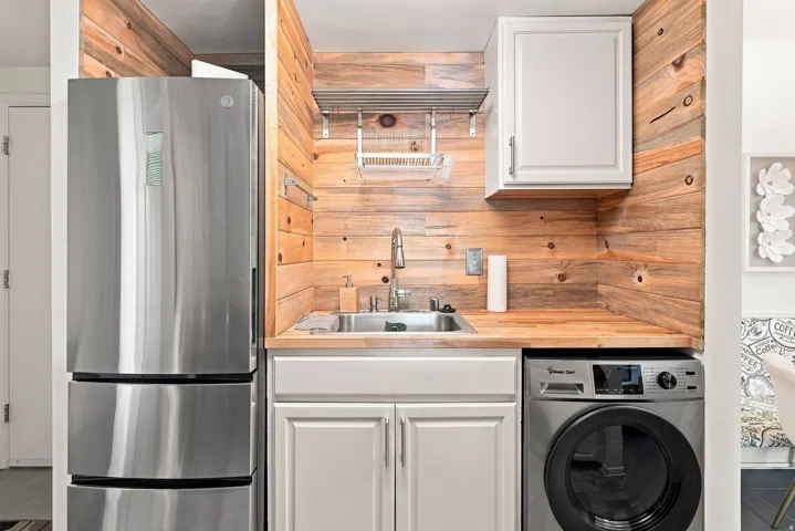 Stainless steel refrigerator, integrated washer, wood-finish countertop, stainless steel sink, and wood-finish paneling