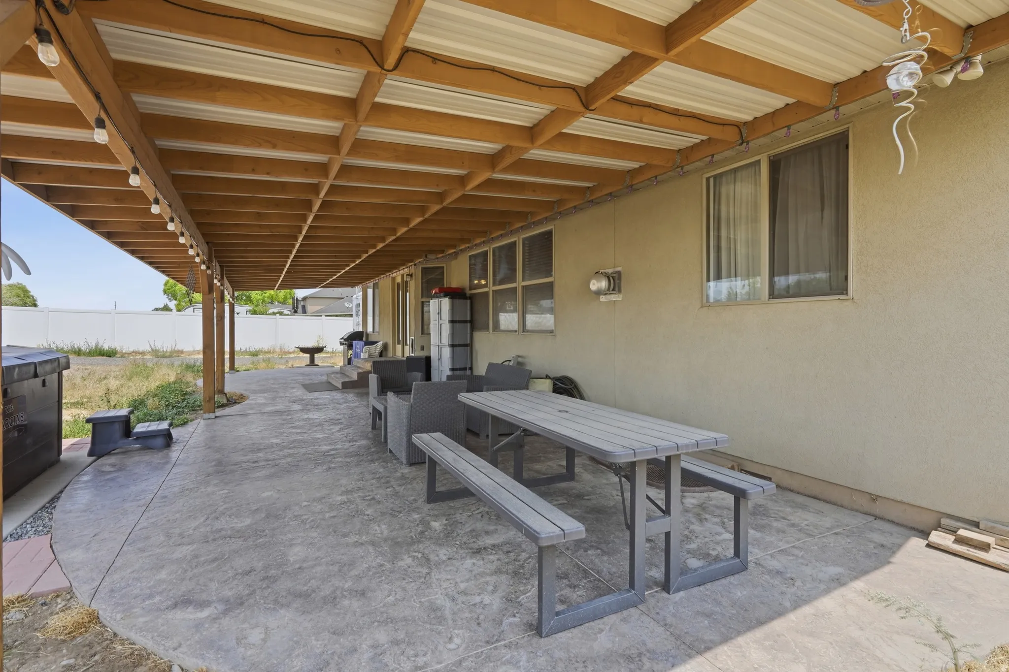 Expansive covered patio featuring a corrugated metal roof supported by wood beams, a stamped concrete surface, and string lighting