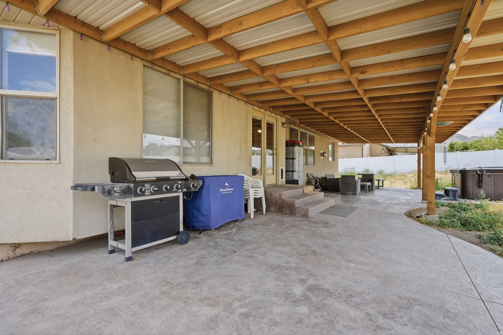 Expansive covered patio featuring a wood-beam ceiling, stamped concrete flooring, and direct access to the interior via double doors