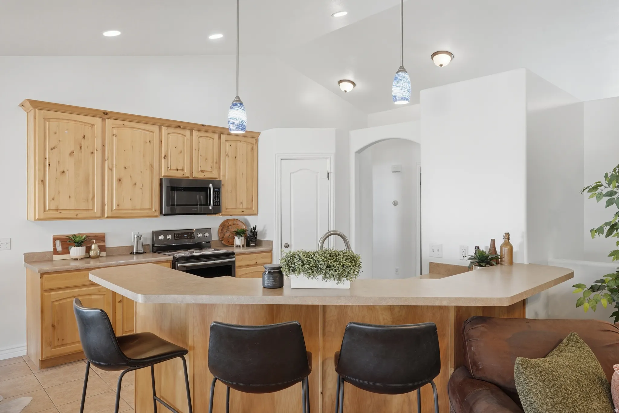 Kitchen featuring light wood cabinetry, dark appliances, a peninsula with a breakfast bar, and pendant lighting