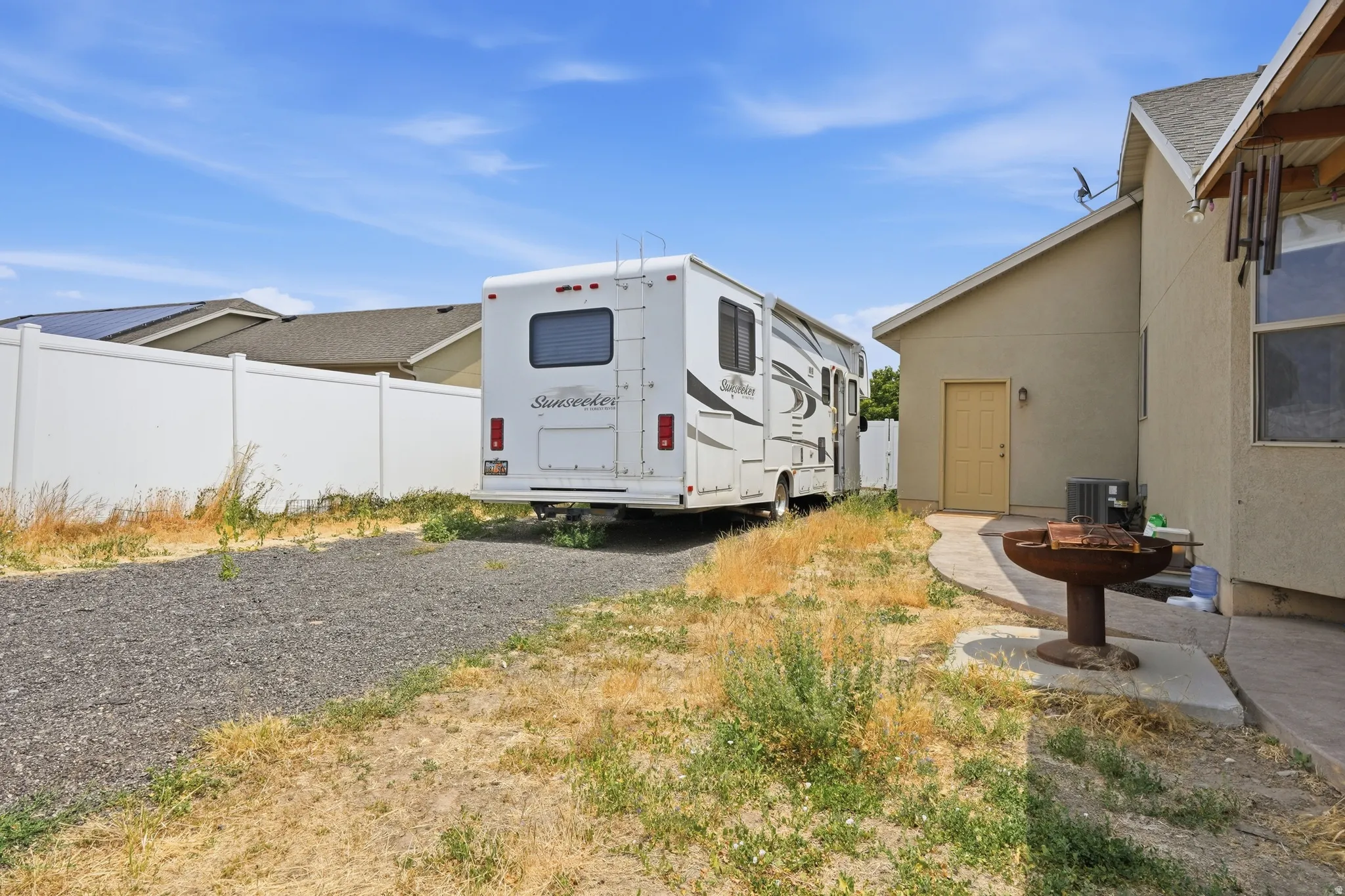 Backyard featuring a gravel parking area, a white vinyl fence, and a concrete patio