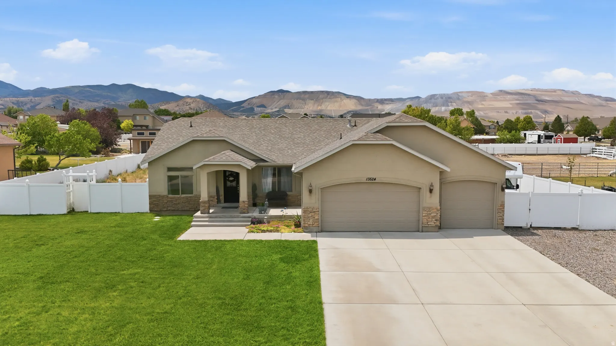 Single-story residence featuring a two-car garage, stone and stucco exterior, and a white vinyl fence enclosing the property