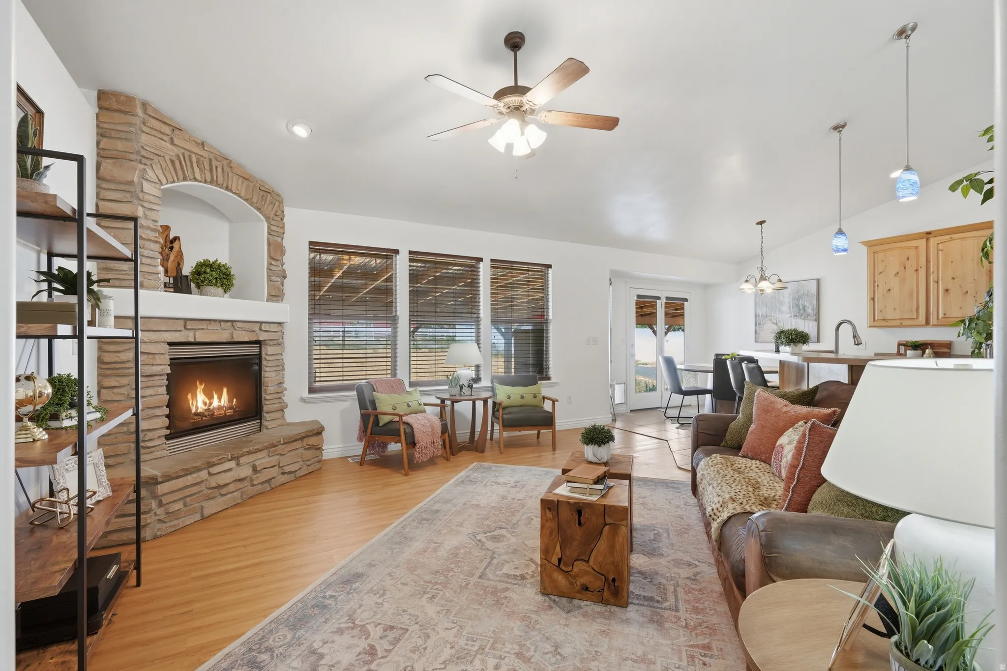 Living room featuring a stacked stone fireplace with an arched niche, wood-finish flooring, and a ceiling fan