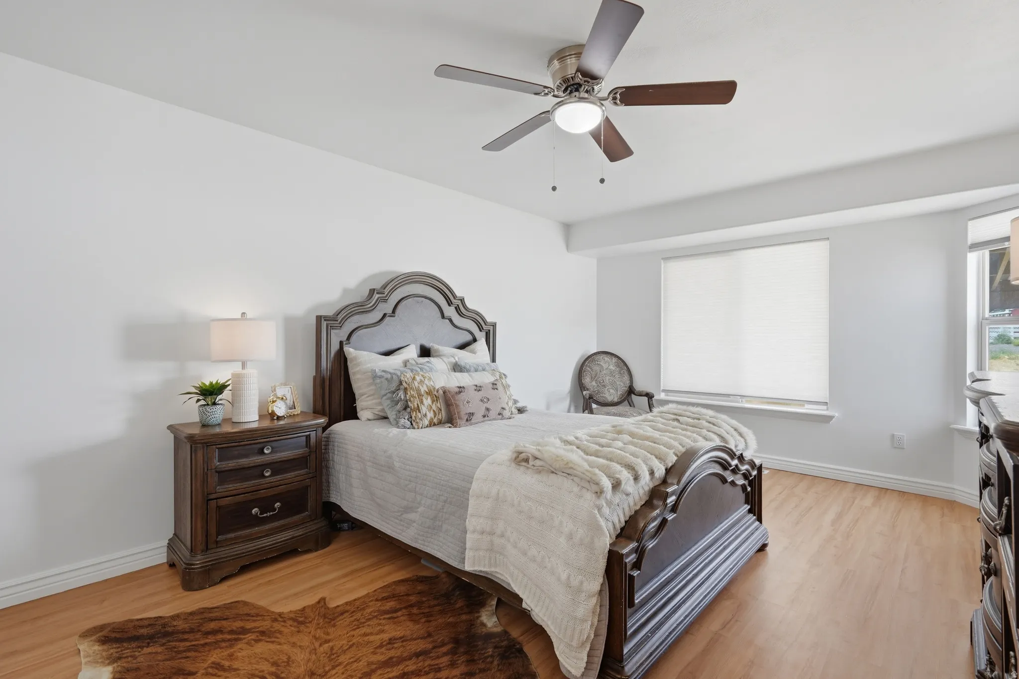 Bright room featuring wood-finish flooring, white walls, and a ceiling fan with integrated lighting