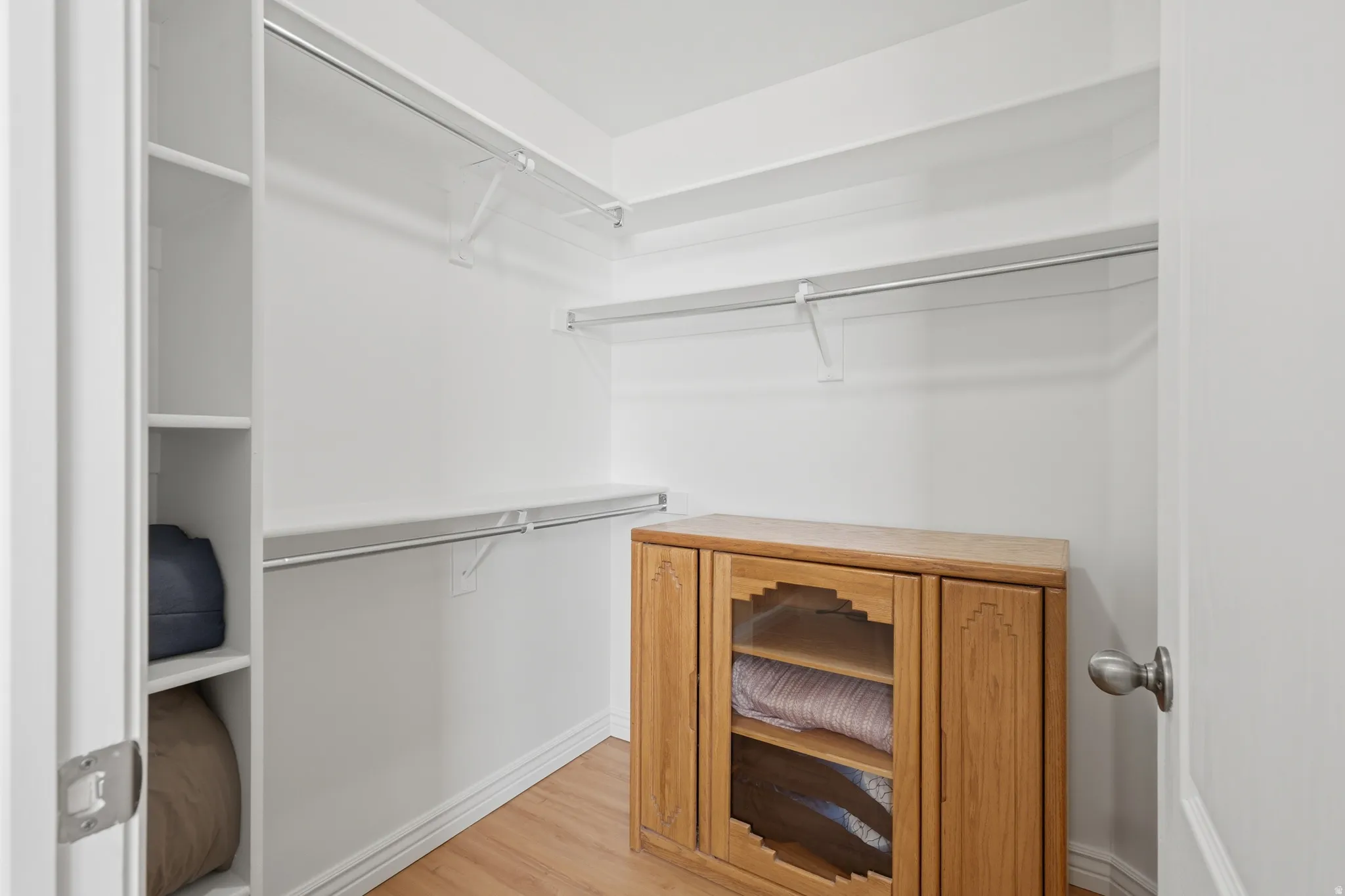 Walk-in closet featuring white shelving, multiple hanging rods, and wood-finish flooring