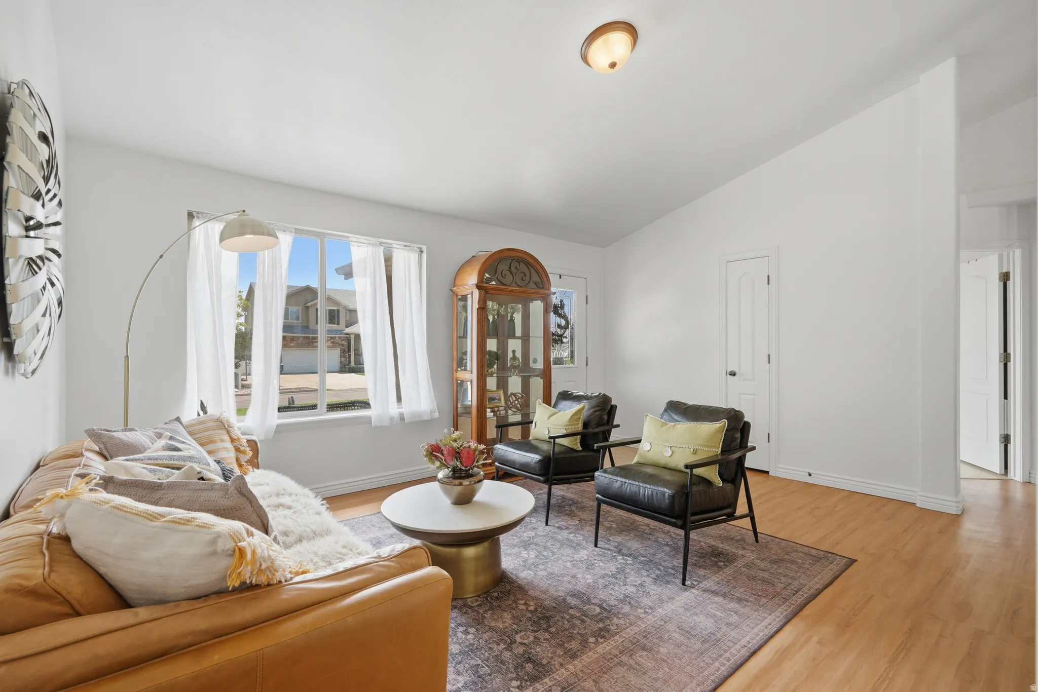 Bright living area featuring a large window with white sheer curtains, light wood-finish flooring, and white painted walls