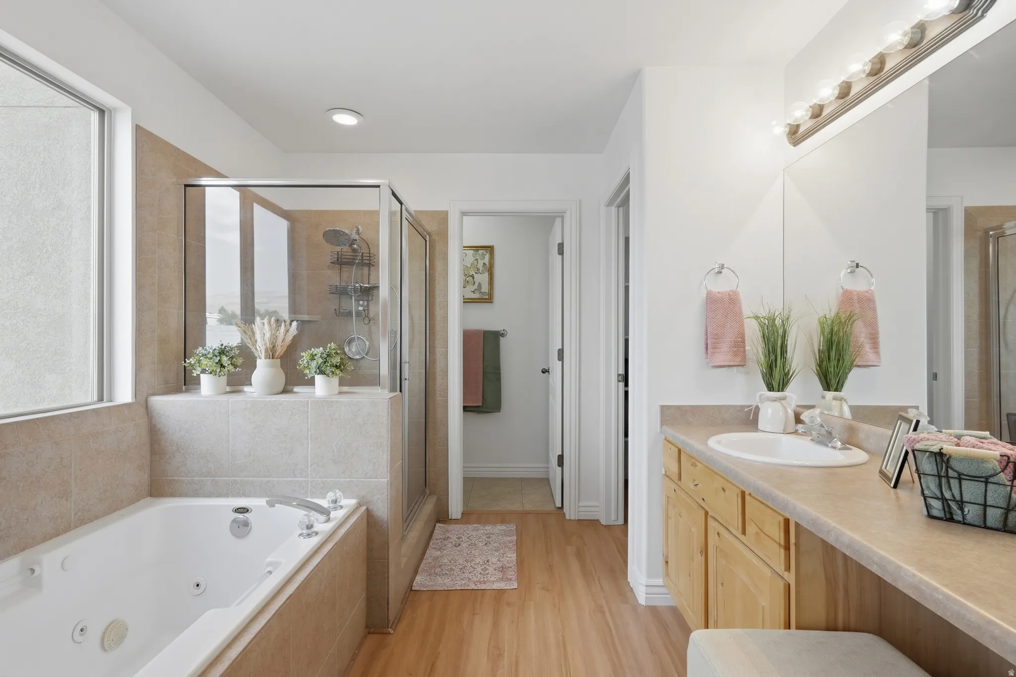 Bathroom featuring a jetted soaking tub, glass-enclosed shower, light wood-finish flooring, and a vanity with an integrated sink and mirror