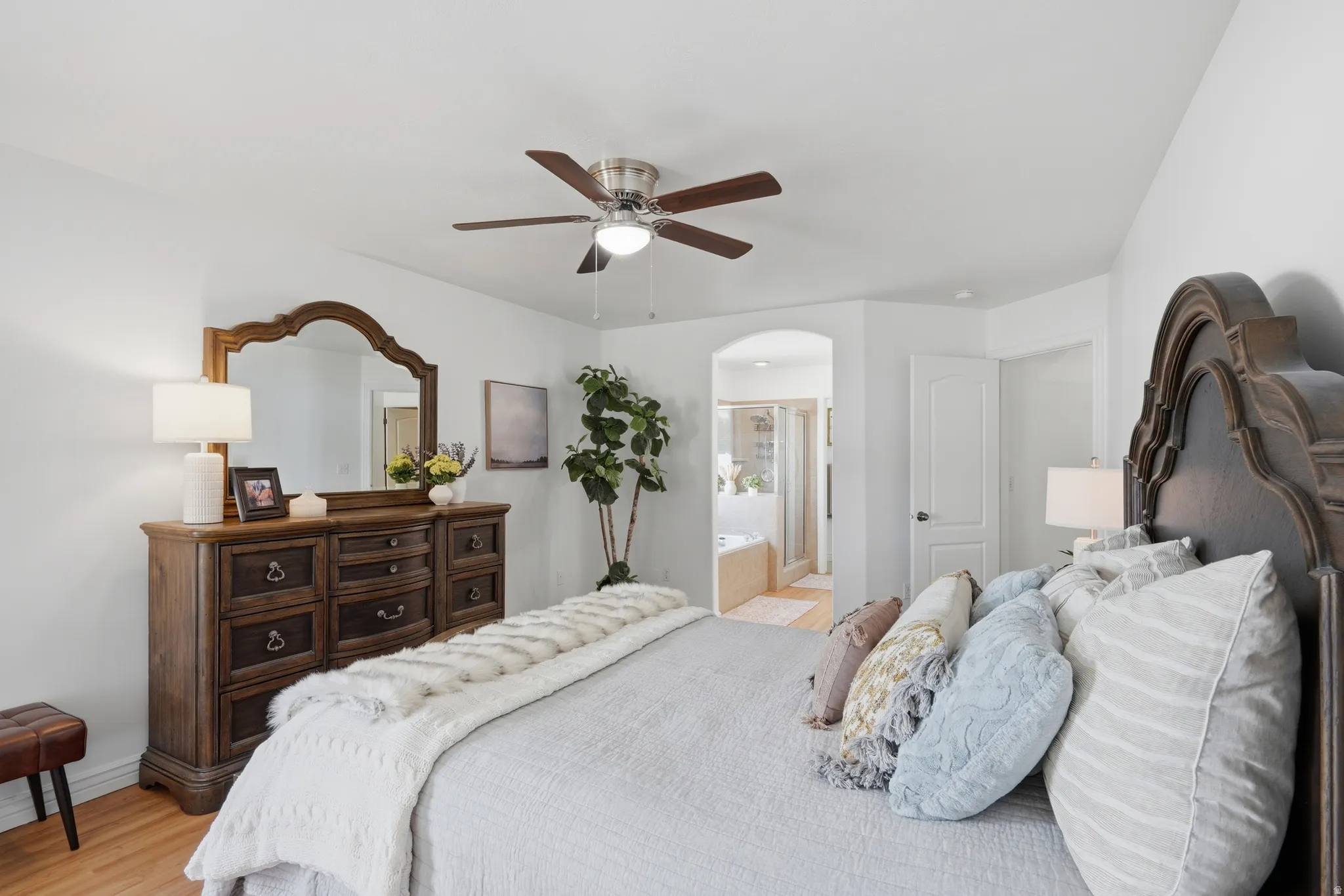 Bedroom featuring wood-finish flooring, a ceiling fan, and an arched doorway leading to a bathroom with a built-in tub