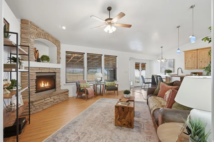 Living room featuring a stacked stone fireplace with an arched niche, wood-finish flooring, and a ceiling fan