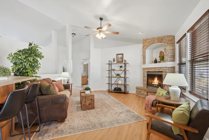 Spacious living area featuring vaulted ceilings, wood-finish flooring, a corner fireplace with stone surround, and multiple windows