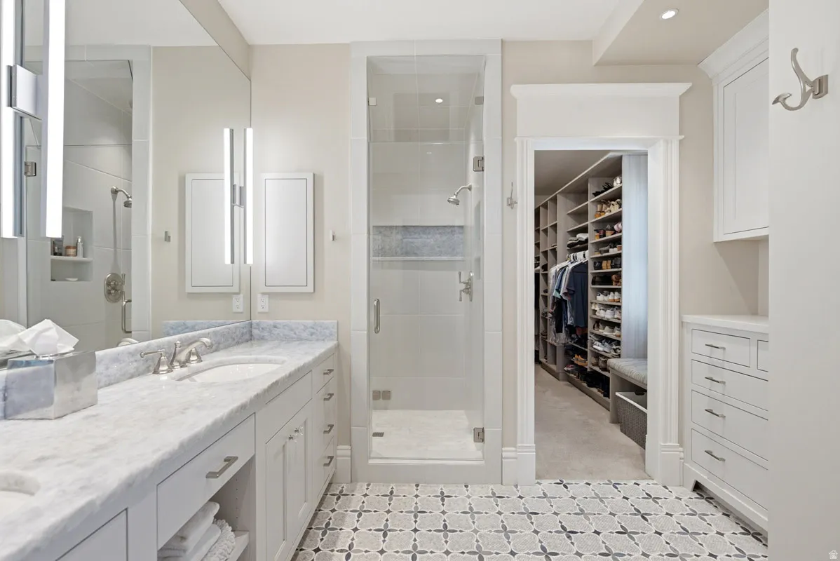 Bathroom featuring a dual-sink vanity with a stone countertop, a glass-enclosed shower, built-in cabinetry, and patterned floor tile