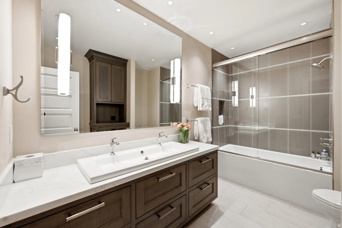 Bathroom featuring a double vanity with stone countertop, dark wood-finish cabinetry, and an expansive mirror