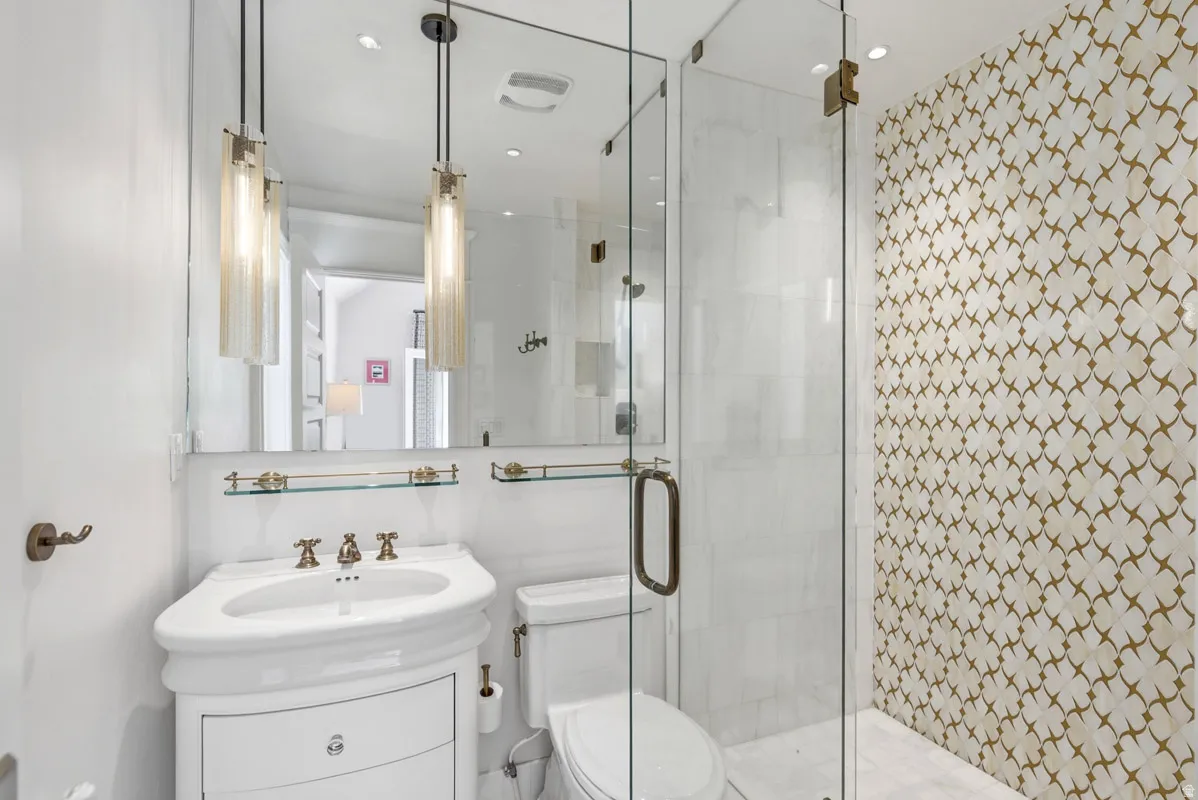 Bathroom featuring a glass-enclosed shower, decorative wall tiling, pedestal sink, and pendant lighting fixtures