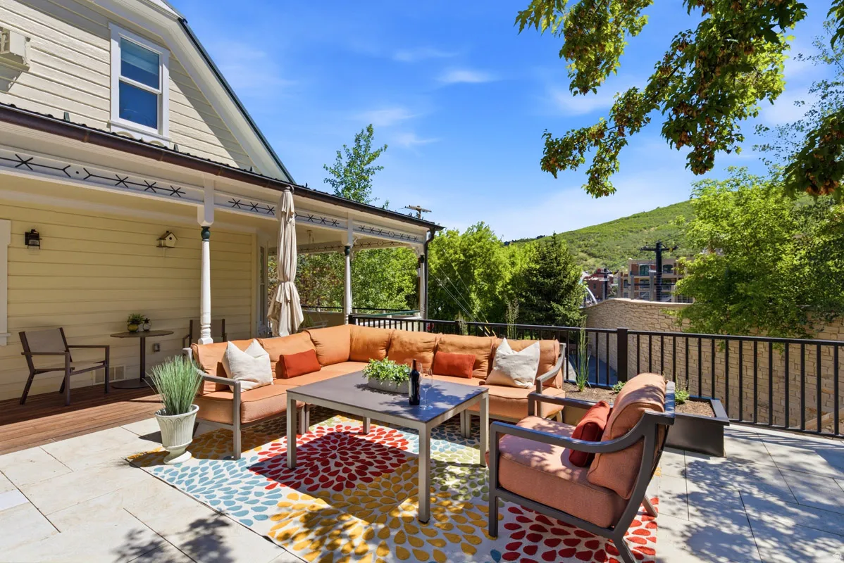 Expansive outdoor patio featuring a stone-paved section, a covered porch with decorative millwork, and a dark metal railing system