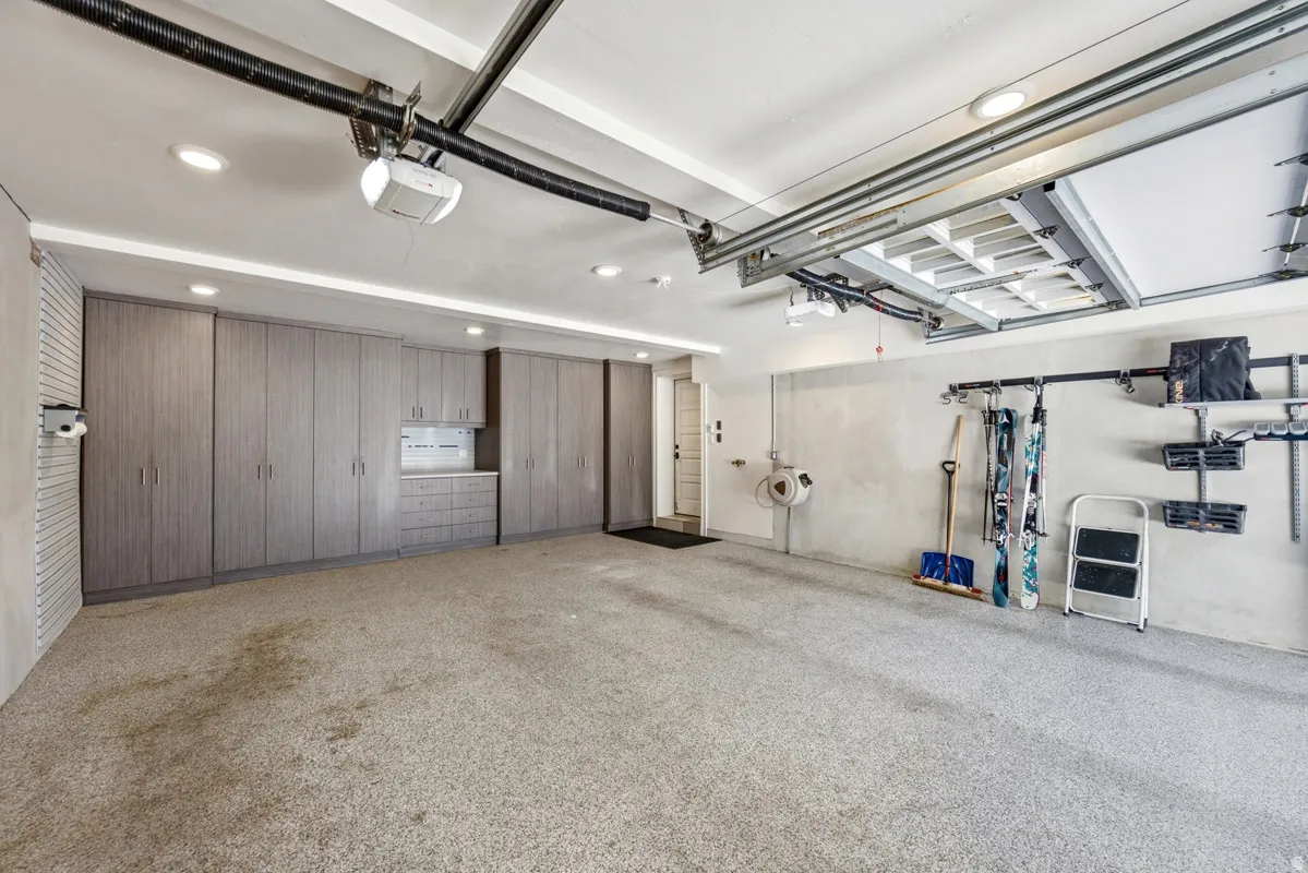 Spacious garage featuring extensive built-in cabinetry, overhead lighting, epoxy flooring, and wall-mounted organization systems