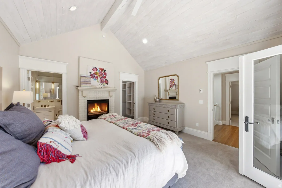 Vaulted ceiling with white wood-paneling, fireplace with tile surround, carpeted flooring, and a built-in shelving unit