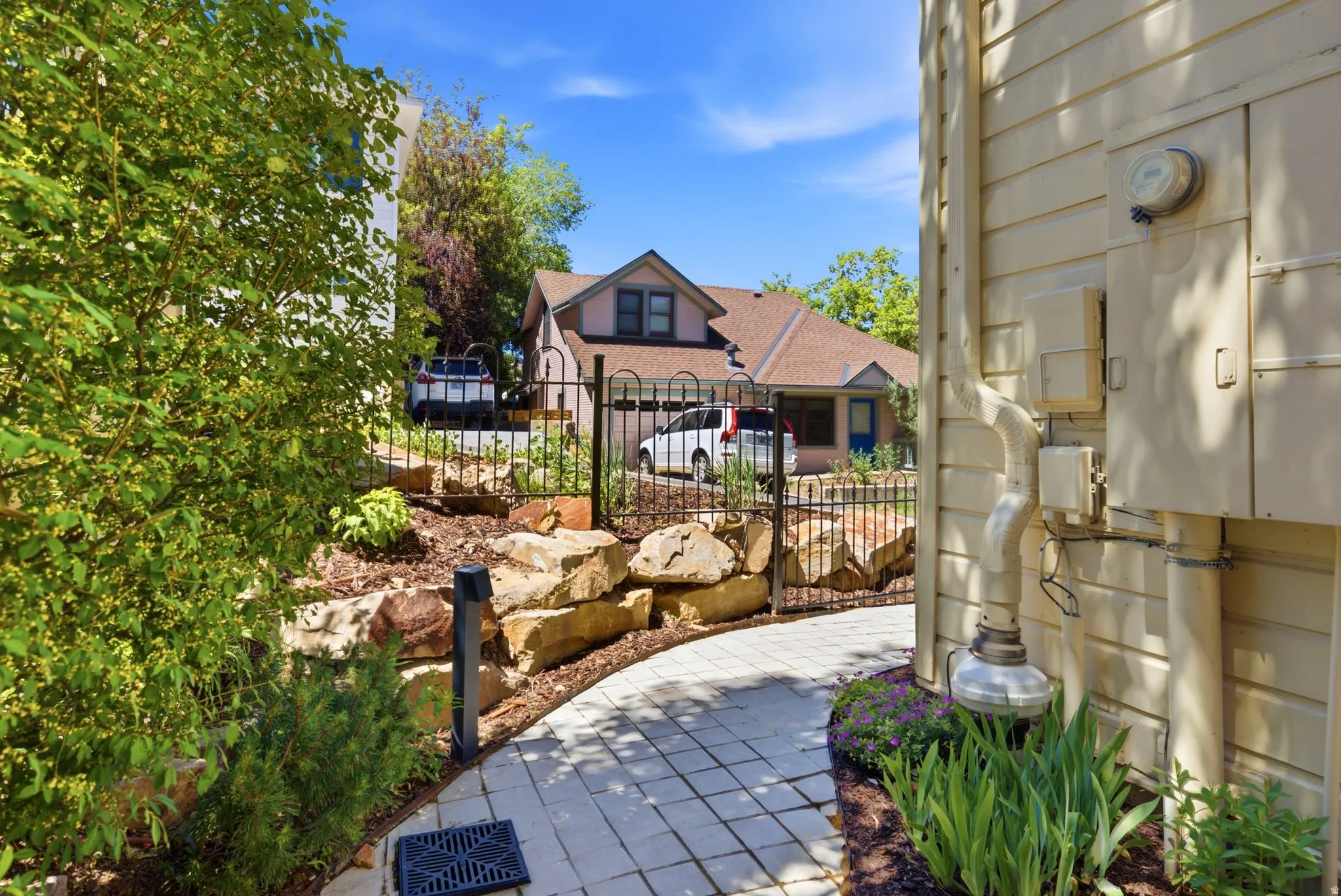 Exterior featuring beige siding, a paved pathway, a landscaped rock garden, and a black wrought iron fence