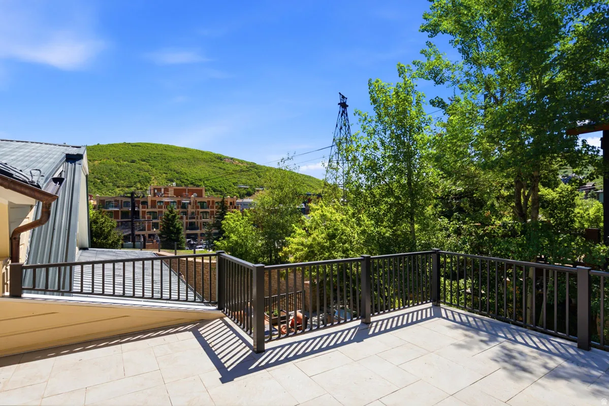 Expansive outdoor terrace featuring light-toned square tile flooring, dark railing, and surrounding lush greenery