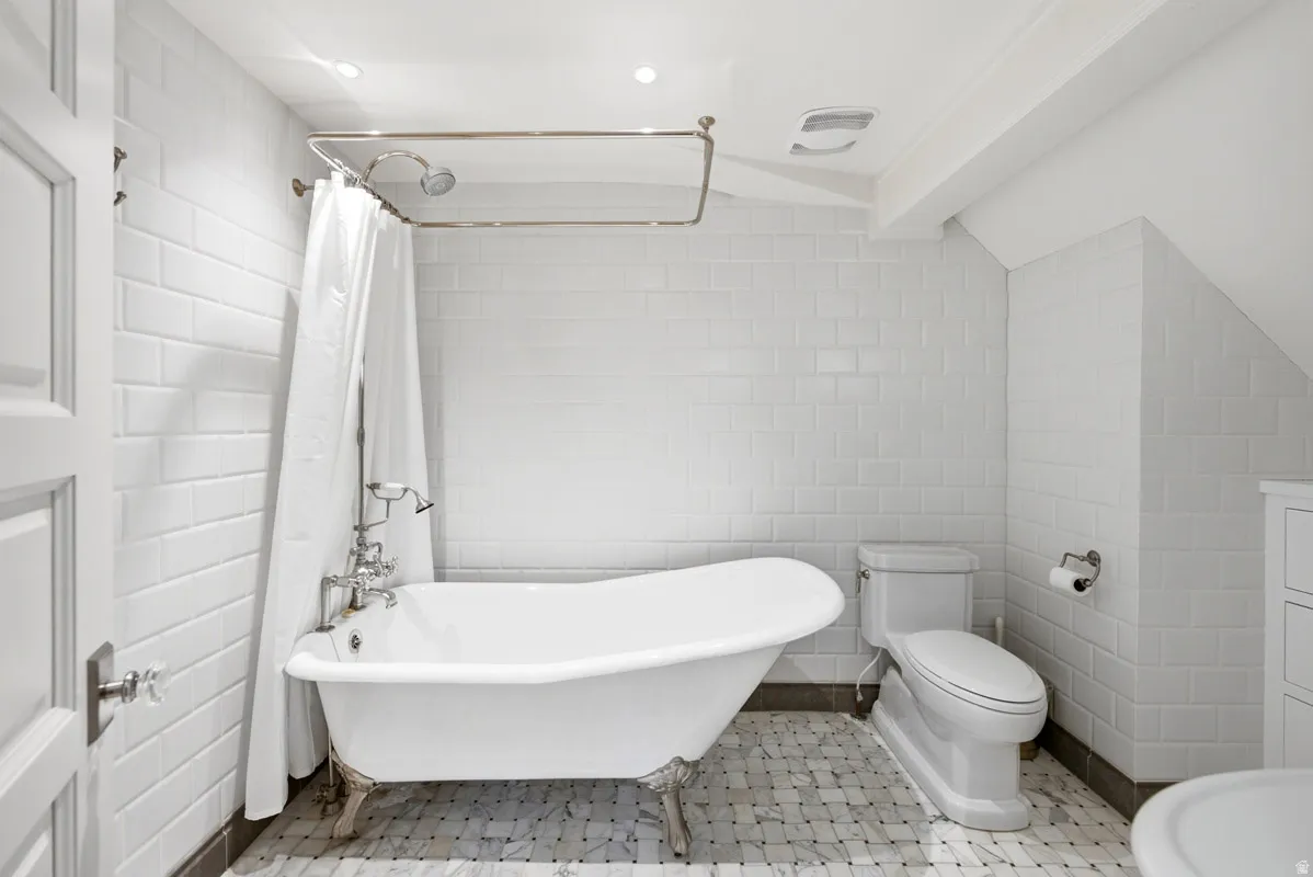 Clawfoot tub with polished chrome fixtures, white subway tile walls, and mosaic tile flooring