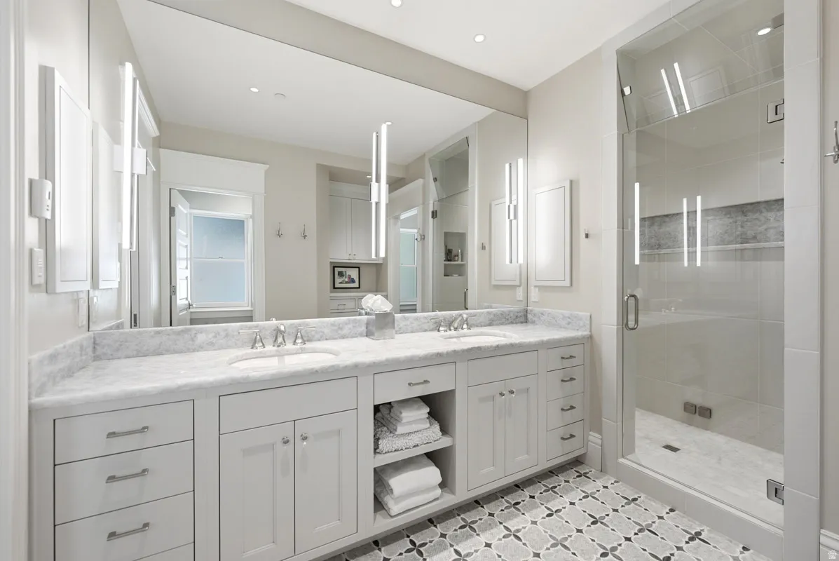 Dual vanity with undermount sinks, stone countertop, custom cabinetry, and patterned floor tile