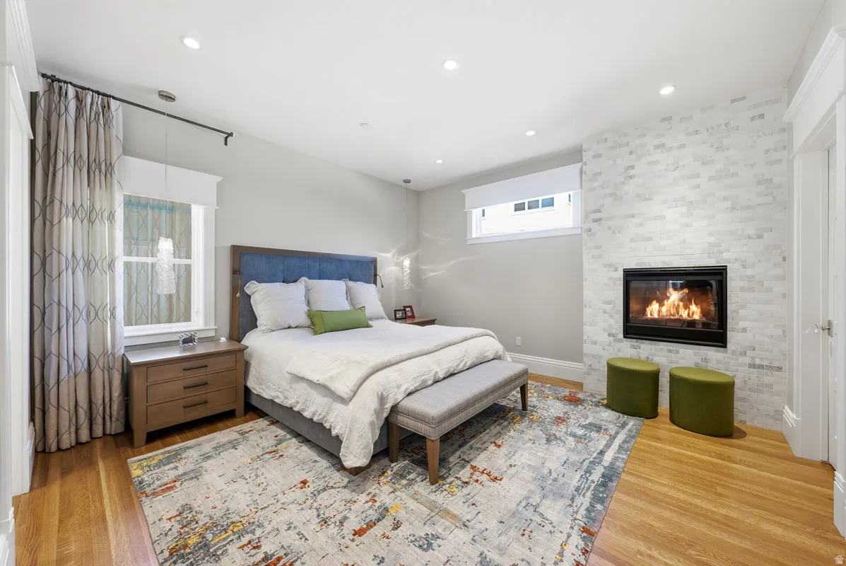 Recessed lighting illuminates this room featuring wood-finish flooring, a white brick-patterned fireplace with black trim, and a window with white trim