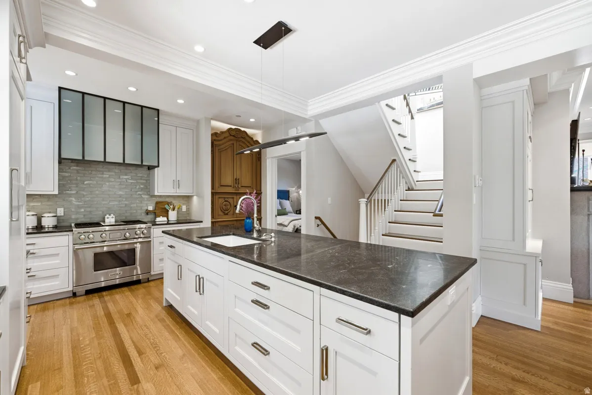 Kitchen featuring a large central island with a dark countertop and undermount sink, white cabinetry with silver-tone hardware, a stainless steel range with a tile backsplash, and wood-finish flooring
