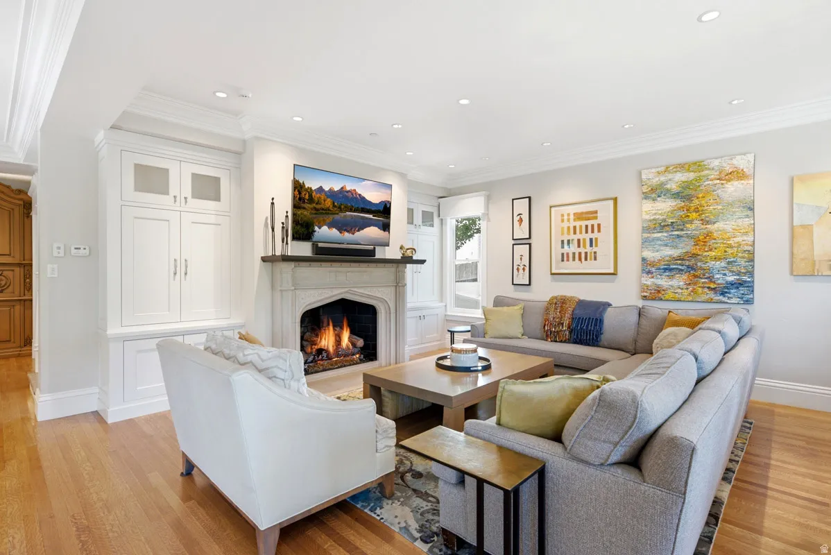 Living area featuring a stone fireplace with a dark mantel, built-in cabinetry, recessed lighting, crown molding, and wood-finish flooring
