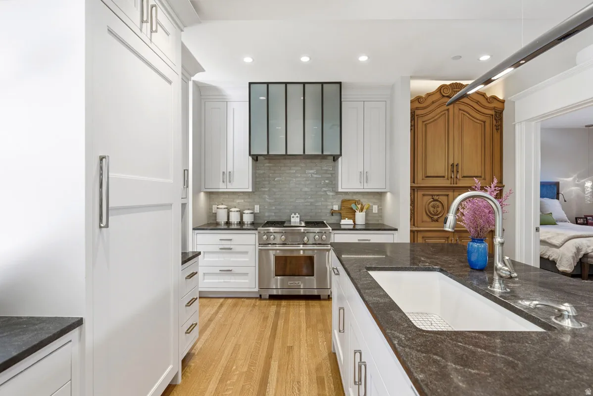 Gourmet kitchen featuring a large island with an undermount sink, stone countertops, stainless steel appliances, a tile backsplash, and wood-finish flooring