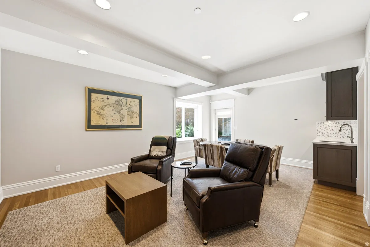Finished basement space featuring recessed lighting, a built-in wet bar with white countertop and wave-patterned tile backsplash, multiple windows, and a combination of carpet and wood-finish flooring