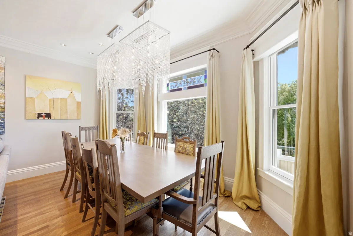 Dining area featuring wood-finish flooring, a rectangular crystal chandelier, and multiple pane windows with an upper stained glass accent