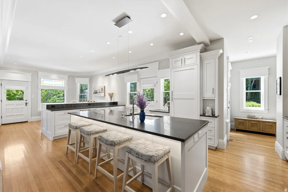 Expansive kitchen featuring a large island with integrated seating, stone countertops, white cabinetry with integrated appliances, recessed lighting, and wood-finish flooring