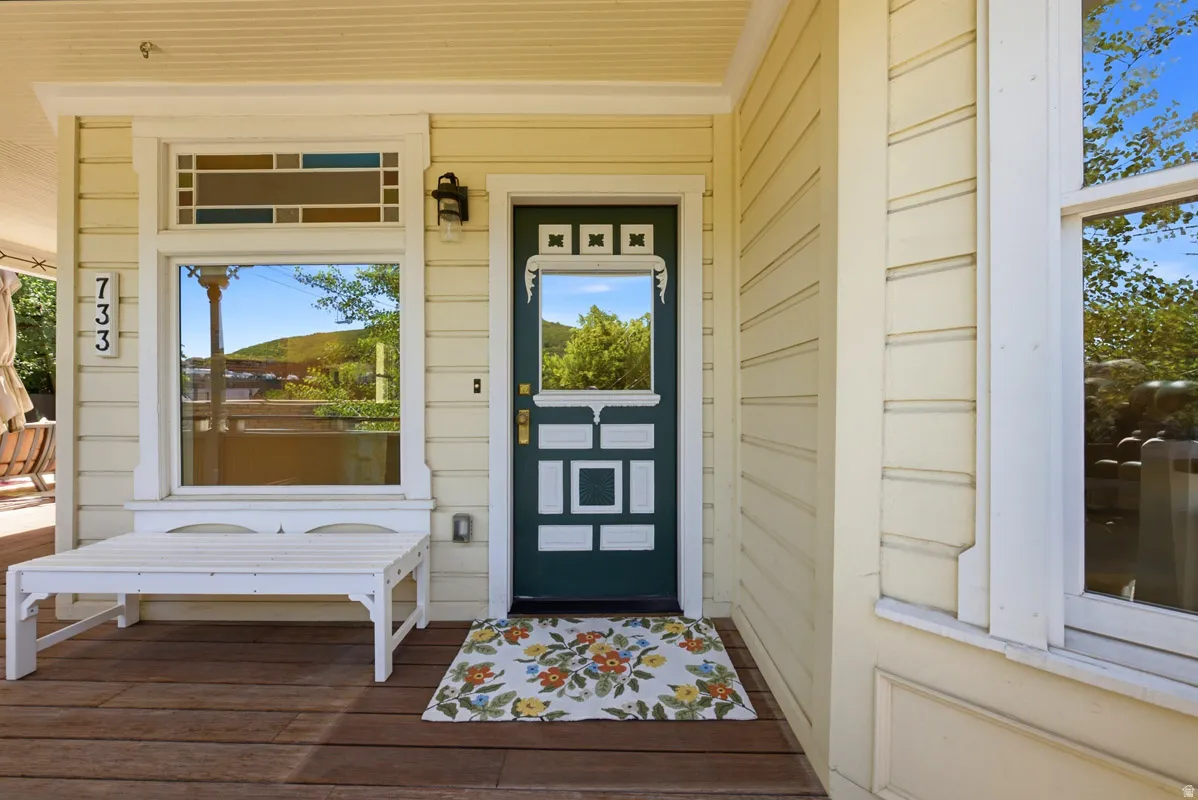 Inviting porch entry featuring a dark green door with decorative white trim, a large window with a transom, wood-finish flooring, and horizontal siding