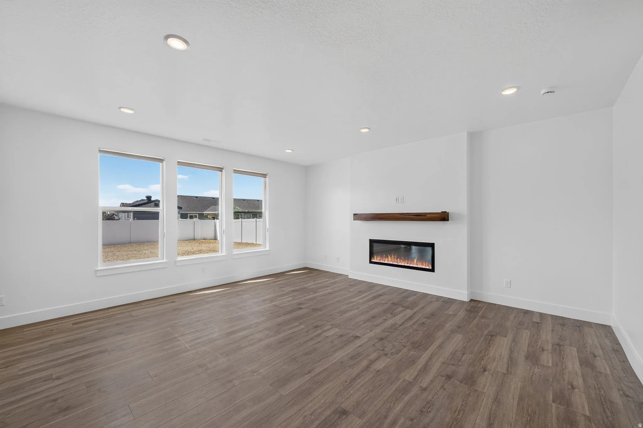 Spacious room featuring wood-finish flooring, recessed lighting, and a built-in electric fireplace with a wood mantle