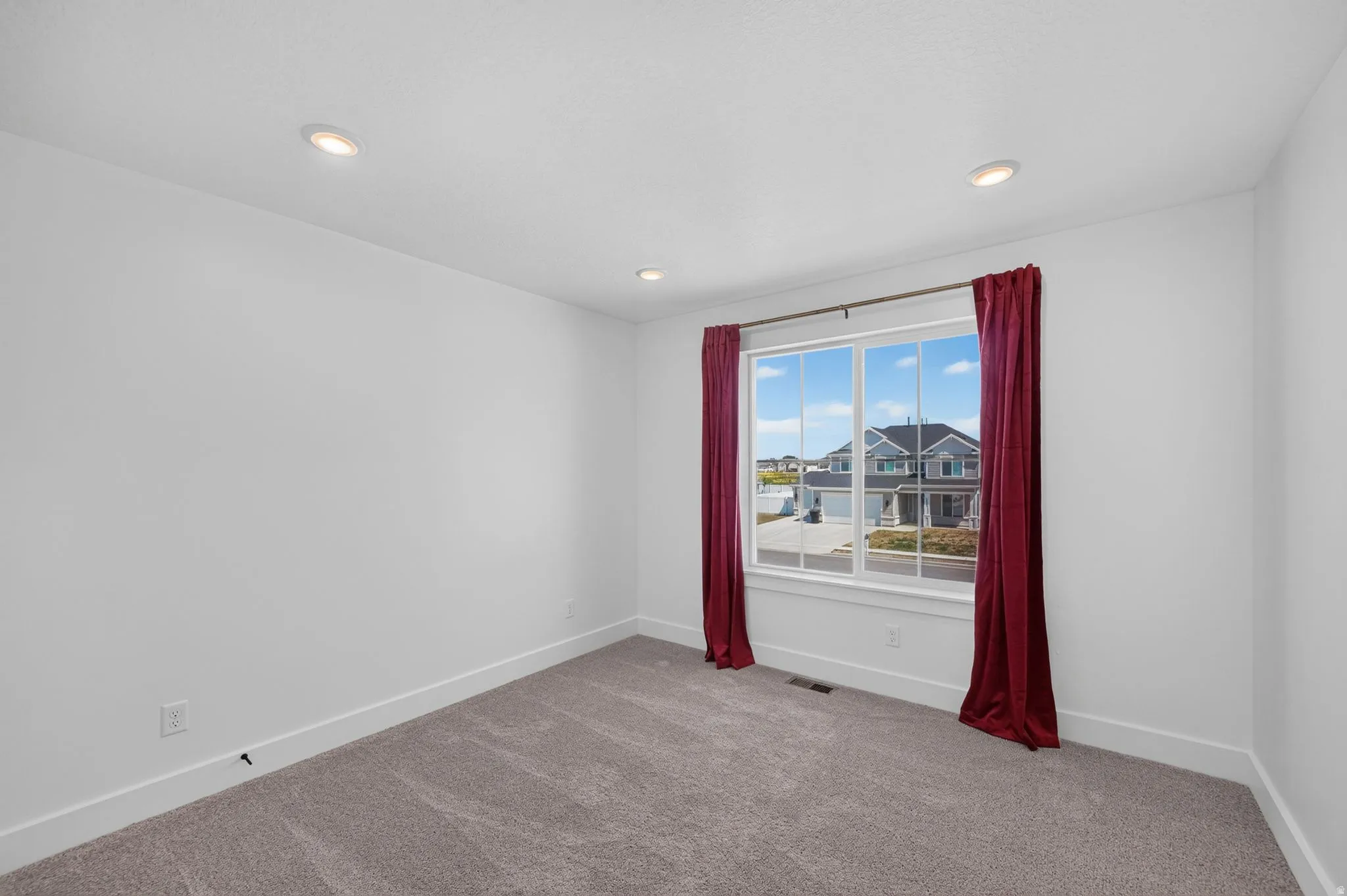 Bright bedroom 2 featuring a large multi-pane window, recessed ceiling lighting, light-colored walls, broad white baseboards, and neutral-toned carpet flooring