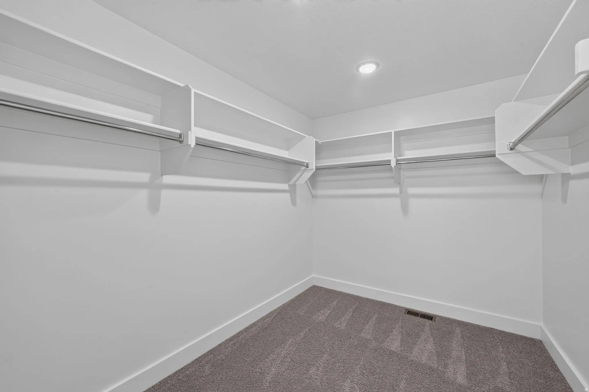 Walk-in closet featuring built-in shelving, integrated hanging rods, recessed ceiling light, white baseboards, and grey patterned carpet flooring