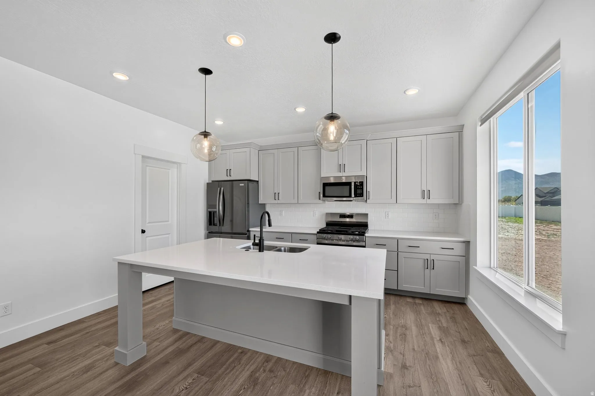 Modern kitchen featuring a central island with a sink, quartz countertops, gray cabinetry, stainless steel appliances, and wood-finish flooring