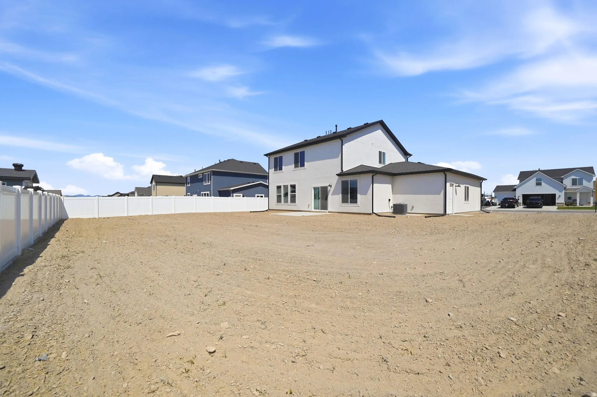 Spacious backyard with a white vinyl privacy fence and a two-story residence featuring a white exterior, black trim, and a patio area