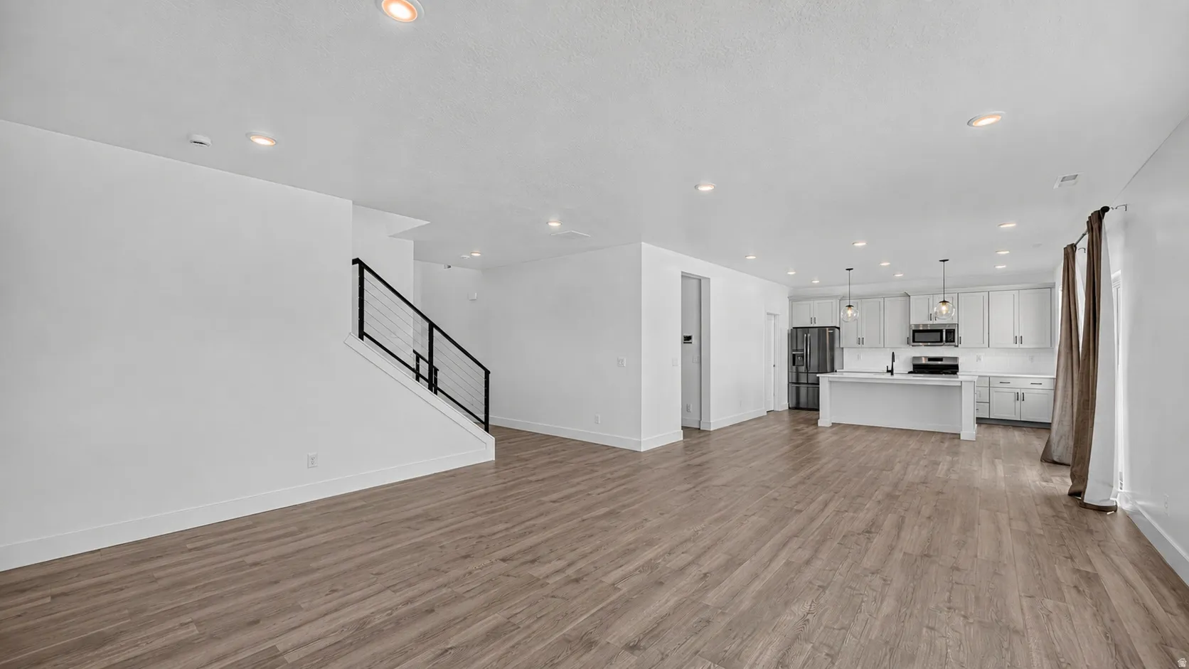 Spacious open-concept living area featuring wood-finish flooring, recessed lighting, and a contemporary staircase with black metal railing