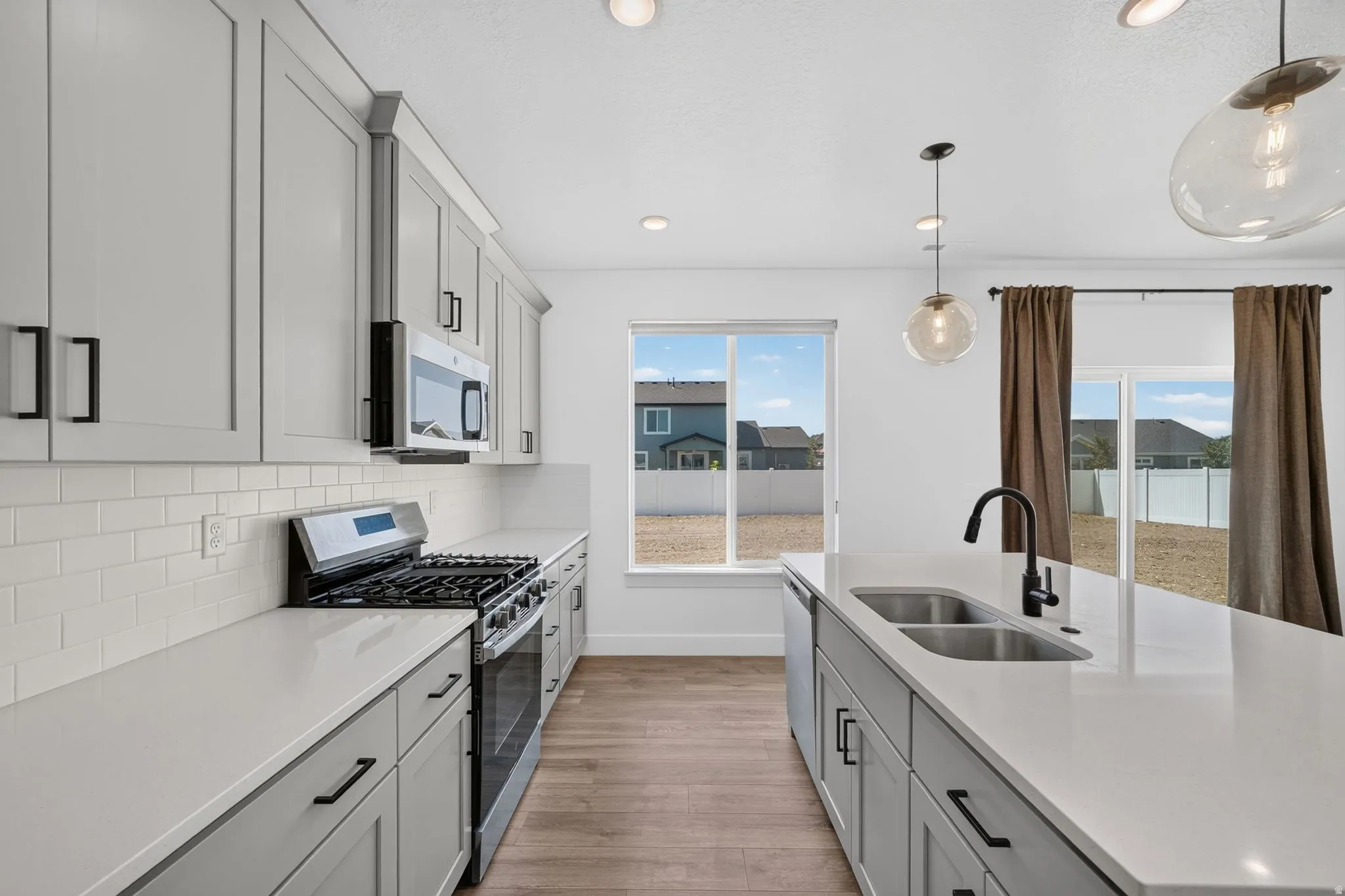 Modern kitchen featuring light gray cabinetry, white countertops, stainless steel appliances, and wood-finish flooring