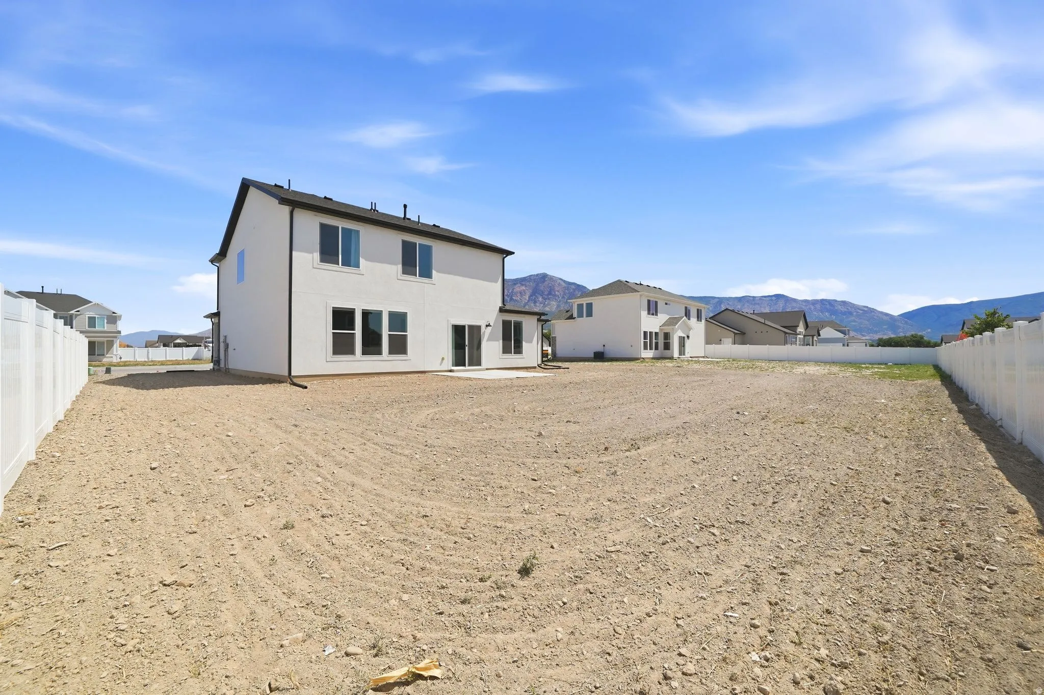 Spacious rear yard featuring a newly constructed residence with a white vinyl fence, a concrete patio, and a mountain backdrop