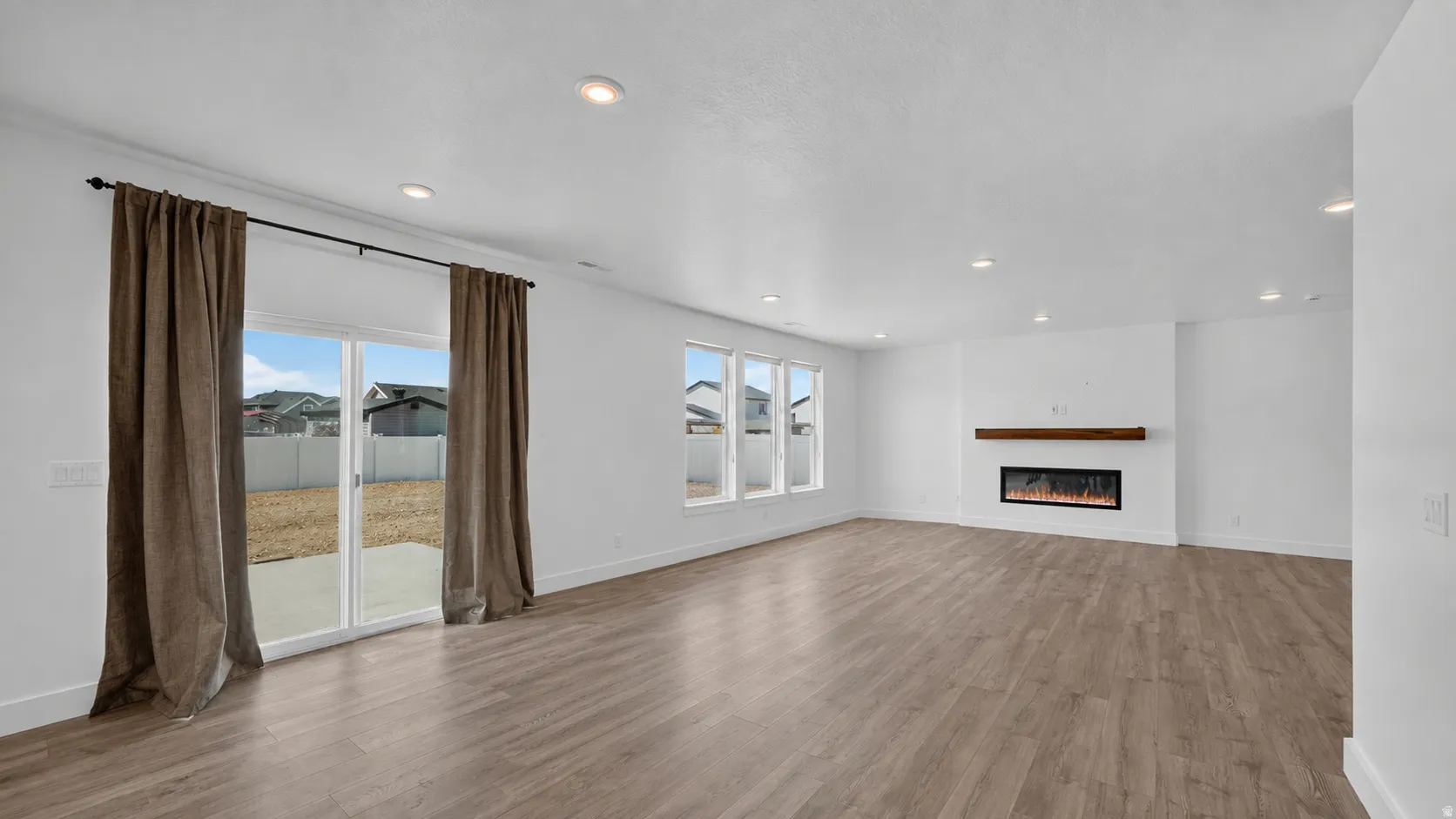 Spacious living area featuring wood-finish flooring, recessed lighting, and a modern electric fireplace with a wood mantle
