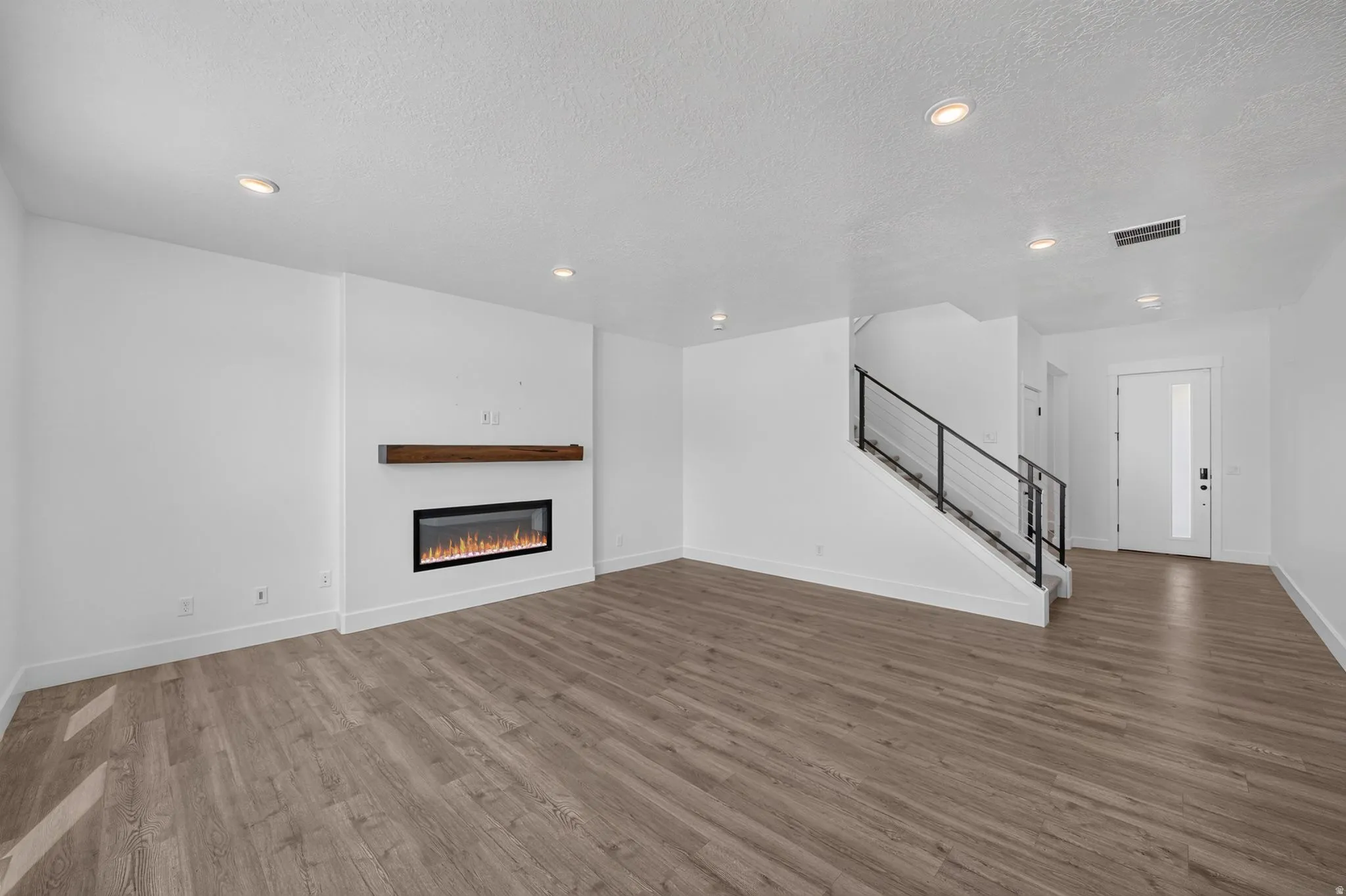 Open-concept living space featuring wood-finish flooring, recessed lighting, and an electric fireplace with a wood mantel