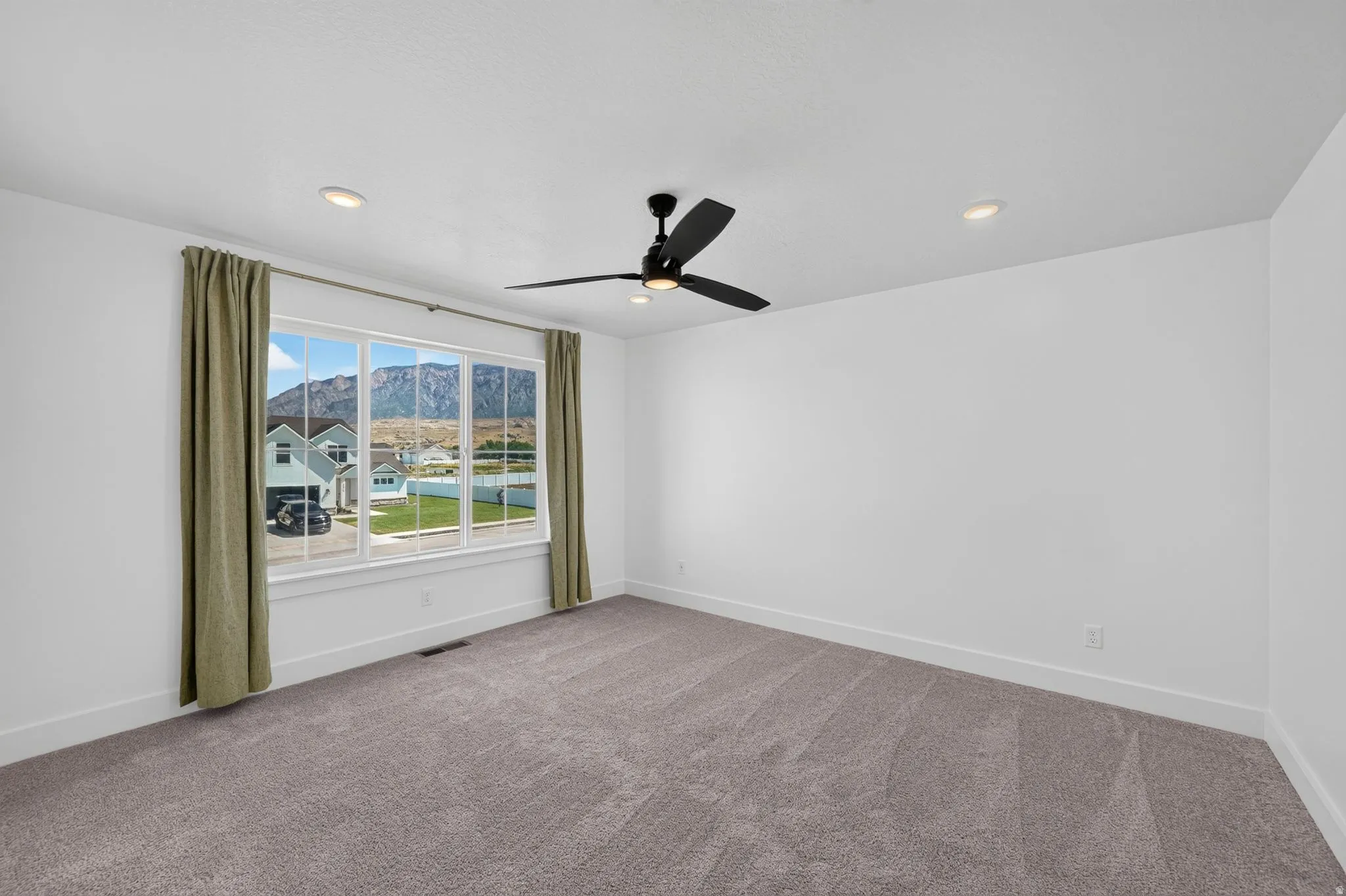Spacious primary bedroom room featuring a large window with mountain scenery, plush grey carpeting, recessed lighting, a ceiling fan, and white baseboards