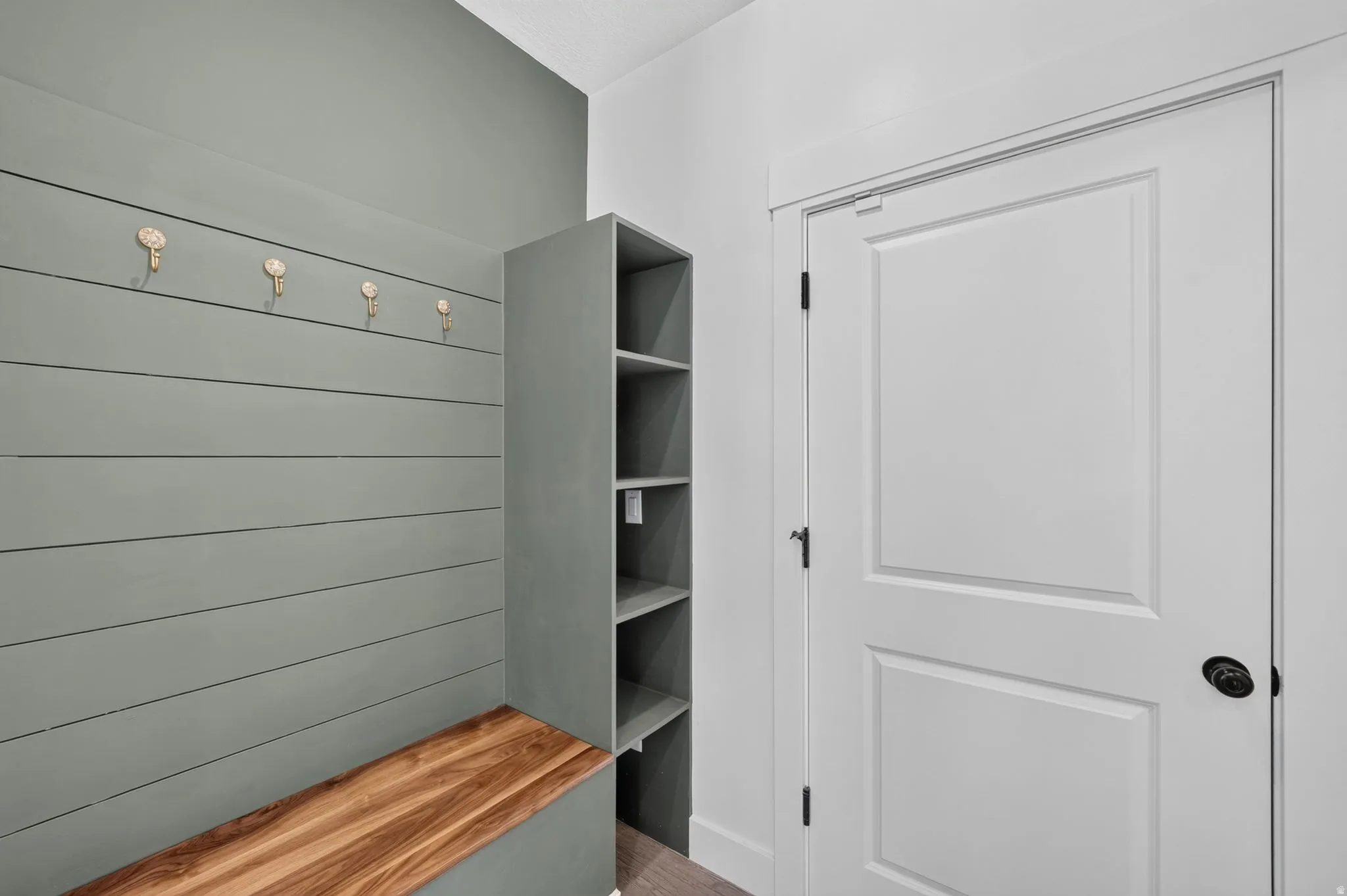 Mudroom featuring shiplap wall paneling, built-in bench with wood surface, custom shelving unit, and decorative wall hooks