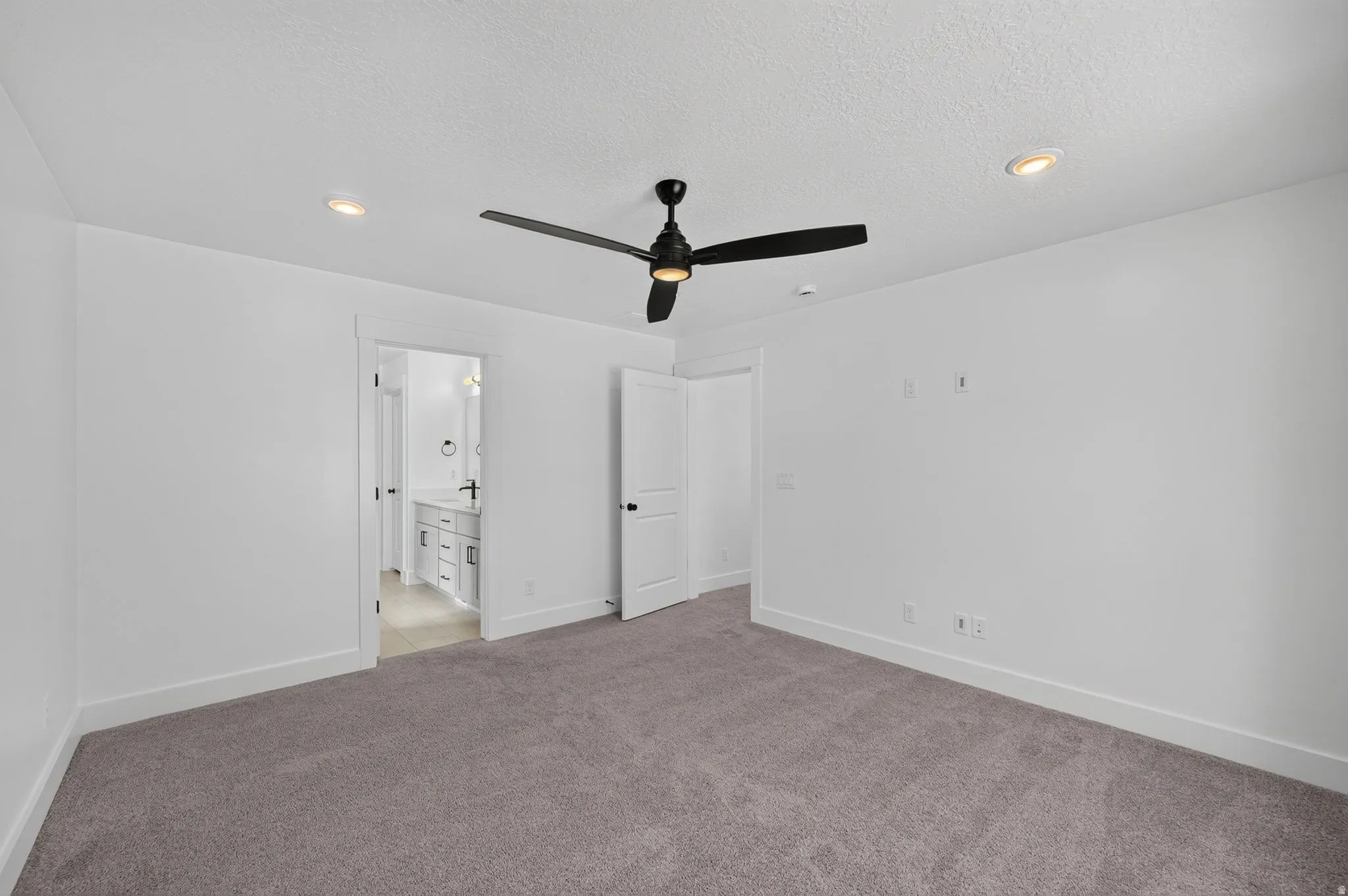 Spacious primary bedroom featuring neutral carpeting, white walls, and a modern ceiling fan