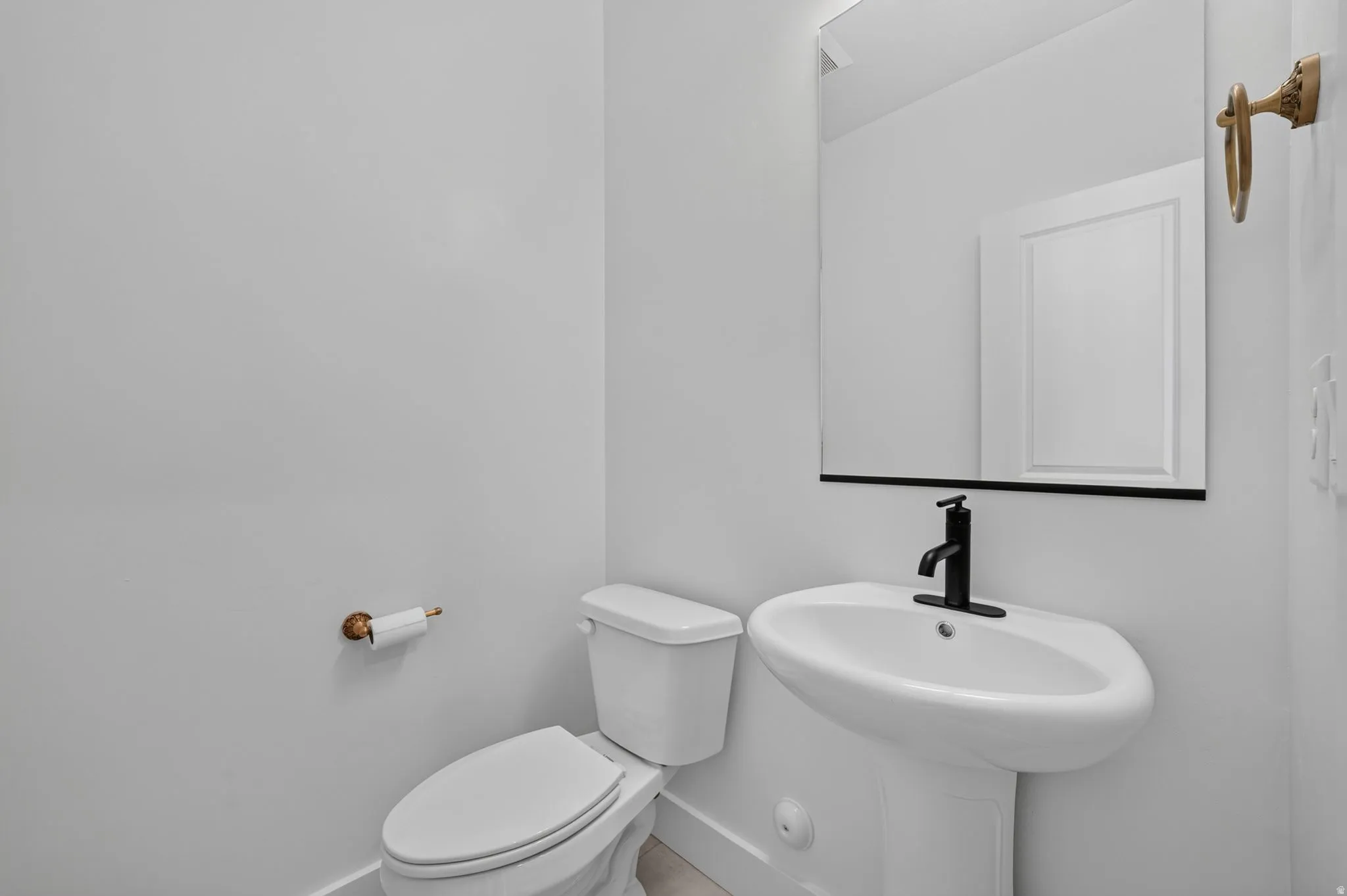 Pedestal sink with a matte black faucet, wall-mounted mirror with a black frame, and a white toilet